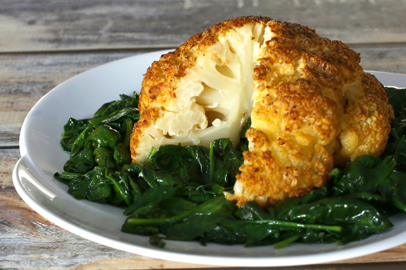 Whole roasted cauliflower on a bed of fresh cooked spinach.