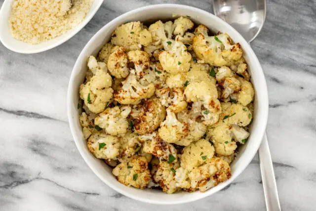 Air fryer cauliflower in a serving bowl with Parmesan cheese on the side.