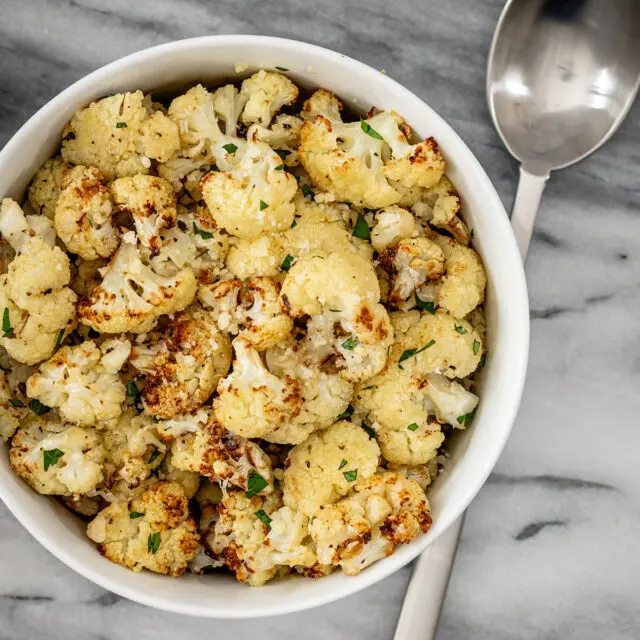 A bowl of air fryer roasted cauliflower ready to eat with parsley garnish.