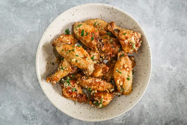 Air fryer chicken wings in a bowl with Parmesan cheese and parsley garnish.