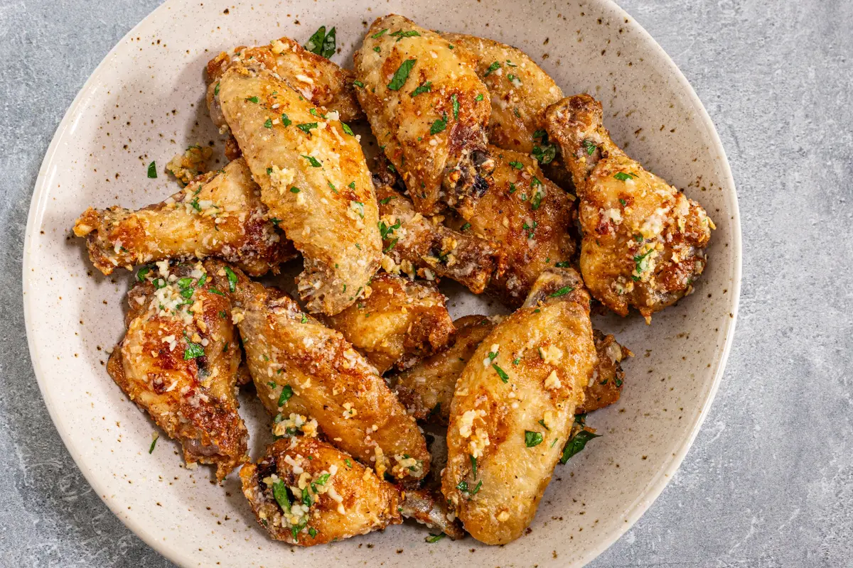 Air fryer chicken wings in a bowl with Parmesan cheese and parsley garnish.