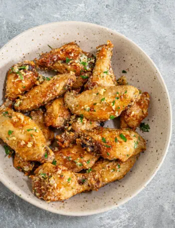 Air fryer chicken wings in a bowl with Parmesan cheese and parsley garnish.