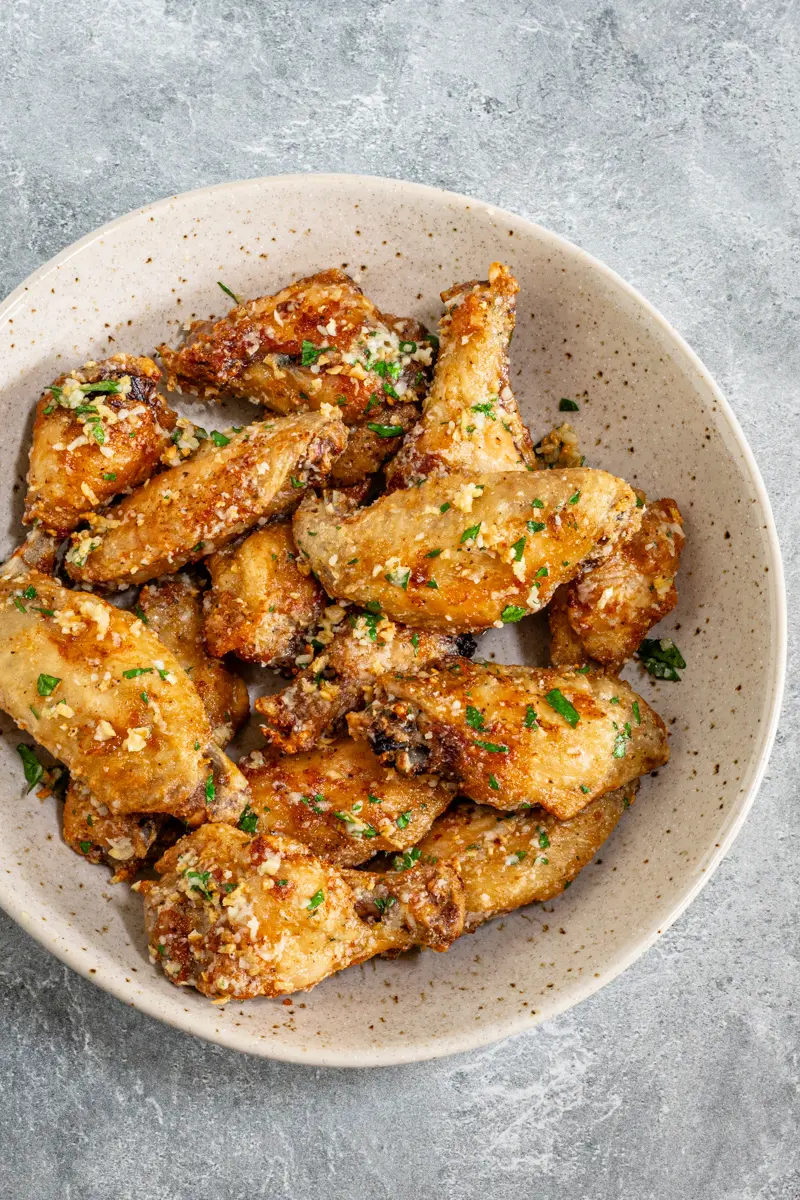 Air fryer chicken wings in a bowl with Parmesan cheese and parsley garnish.