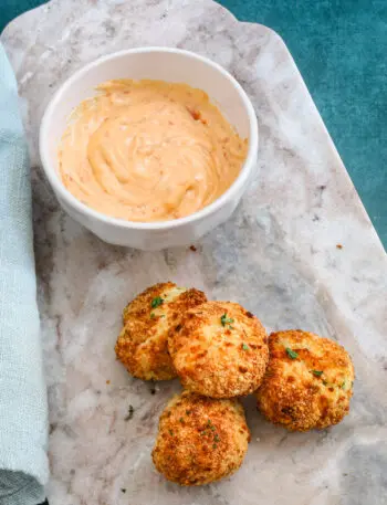 A plate of homemade air fryer potato croquettes made with leftover mashed potatoes, cheese, and herbs, and a dip on the side