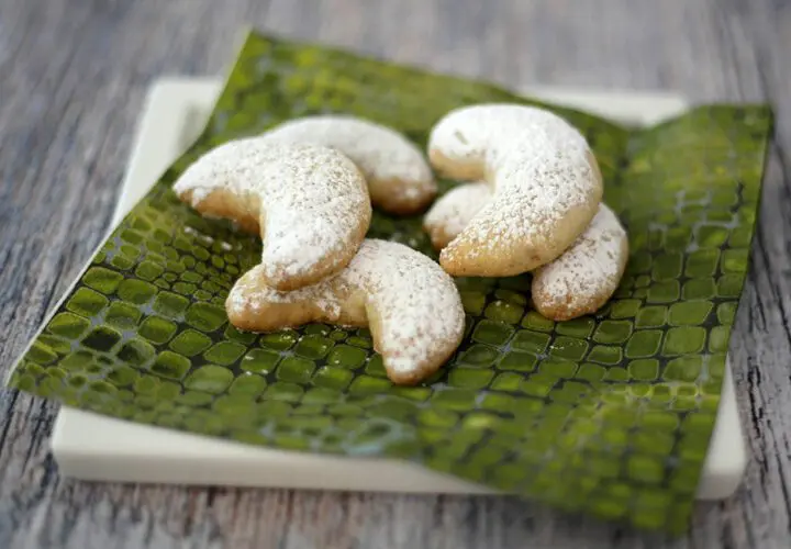 almond crescent cookies on a plate with powdered sugar dusting