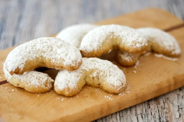 A small cutting board with powdered sugar dusted almond crescent cookies