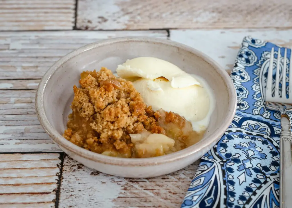 apple crumble with ice cream on a serving dish with a fork on the side.