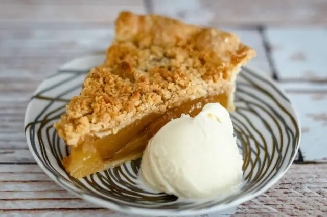 A slice of apple crumble pie with a scoop of ice cream.