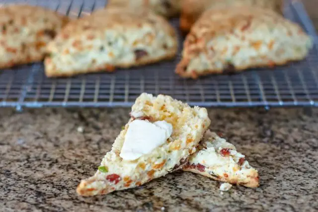 bacon cheddar scones on a cooling rack with one split and buttered