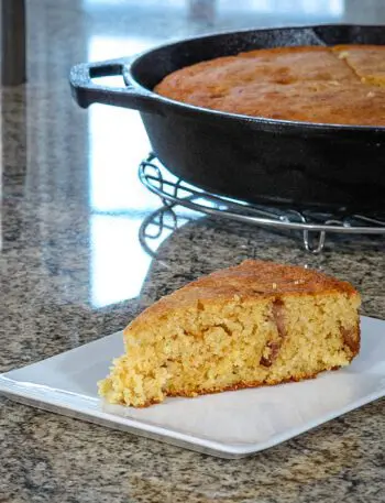 bacon and cheddar cornbread on a plate with the skillet in the background