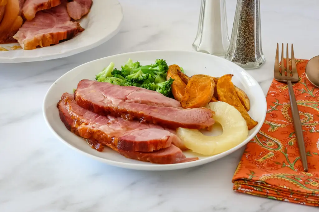 a plate of baked ham with pineapple, sweet potatoes, and broccoli