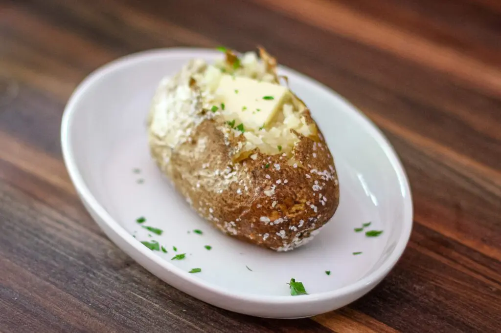 Baked potato on a plate with a pat of butter and some chopped parsley