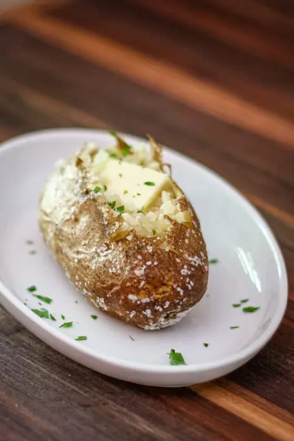 A baked potato on a plate with butter and parsley