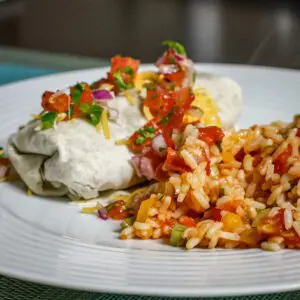 A beef and bean burrito on a plate with a side of Mexican rice and salsa garnish.