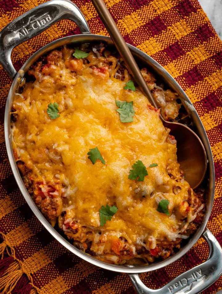 beef and bean taco casserole shown in a pan with melted cheese topping and cilantro leaves