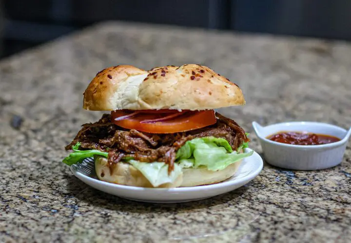 barbecue beef sandwich on a small plate with barbecue sauce on the side.