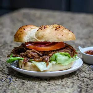 slow cooker barbecued beef shown in a toasted bun with lettuce and tomatoes