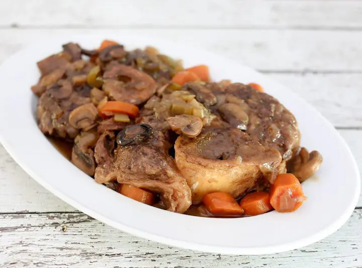 braised beef shanks on a platter with garlic, mushrooms, and carrots