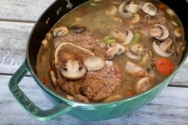 beef shanks in liquids with some sautéed mushrooms and vegetables. Ready to braise in the oven.