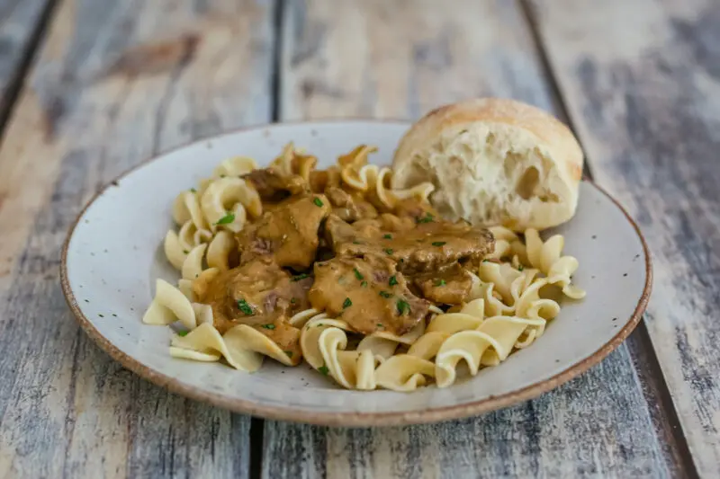 a plate of beef stroganoff over noodles with parsley garnish