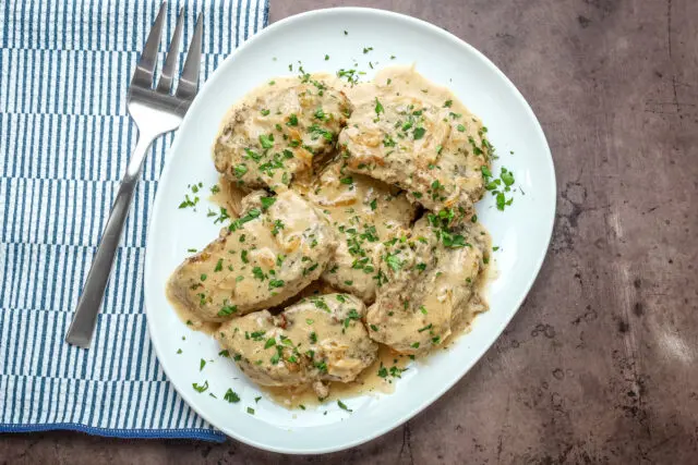 Smothered pork chops on a serving platter with parsley garnish.