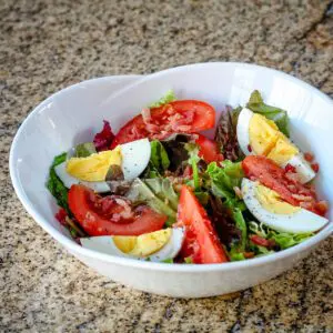 bacon lettuce and tomato salad with hard boiled eggs and vinaigrette, in a large bowl