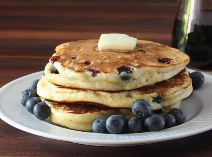 fluffy blueberry pancakes on a plate with butter and fresh blueberries