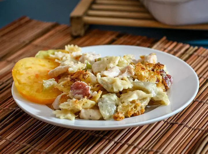 bowtie pasta is shown on a plate with creamy fontina cheese sauce, ham, and sliced tomatoes.