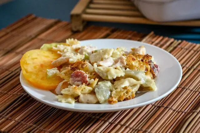 bowtie pasta is shown on a plate with creamy fontina cheese sauce, ham, and sliced tomatoes.