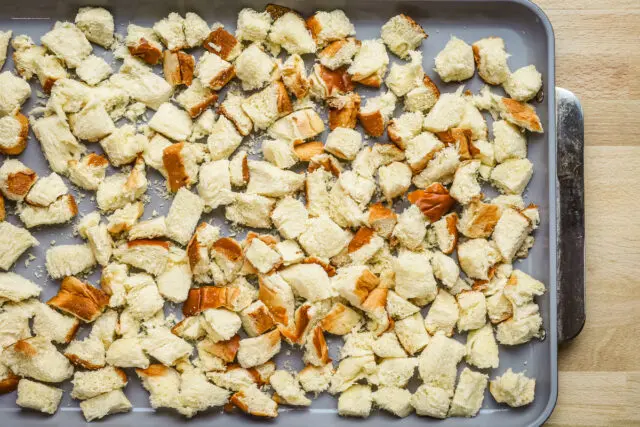 Brioche cubes on a baking sheet ready to dry in the oven to make sausage brioche stuffing.