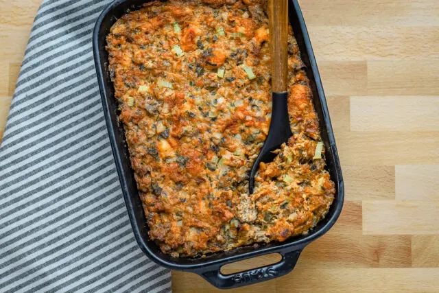 Brioche stuffing in a baking dish with sausage, herbs, and aromatics.