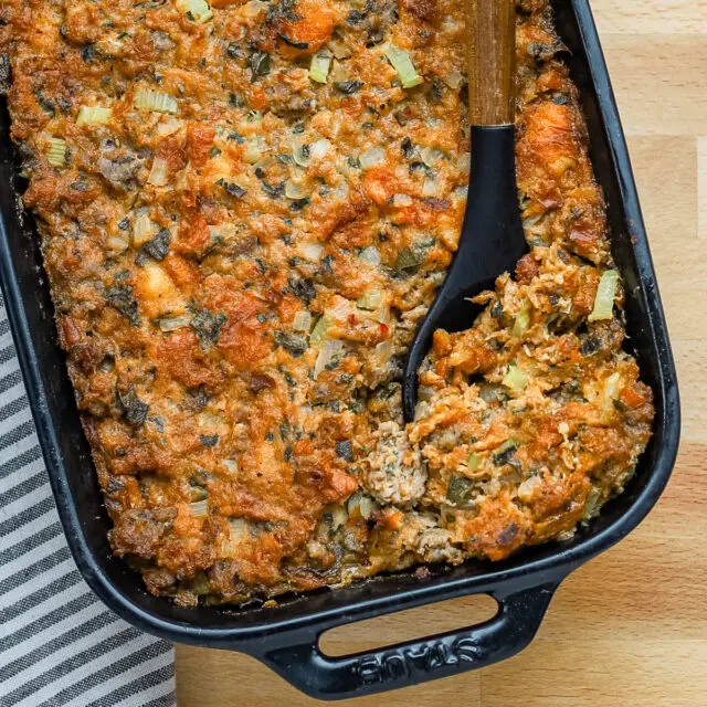 Sausage brioche dressing in a baking dish with a large spoon.