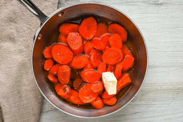 Brown sugar glazed carrots prep: water, butter, and brown sugar are in a pan with sliced carrots.