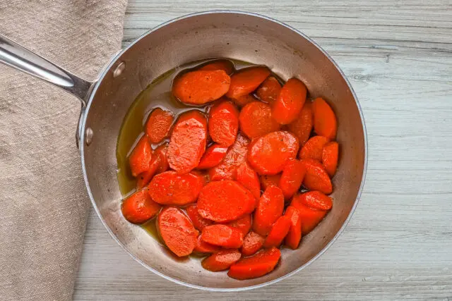 Brown sugar glazed carrots prep: water, butter, and brown sugar are in a pan with sliced carrots.