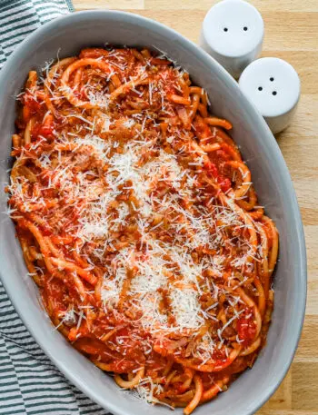 A serving bowl with bucatini all'Amatriciana topped with grated pecorino Romano and extra guanciale.