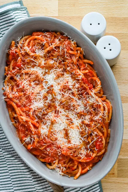 A serving bowl with bucatini all'Amatriciana topped with grated pecorino Romano and extra guanciale.