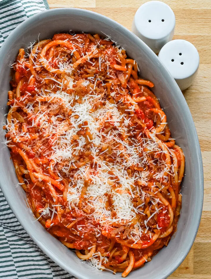 A serving bowl with bucatini all'Amatriciana topped with grated pecorino Romano and extra guanciale.