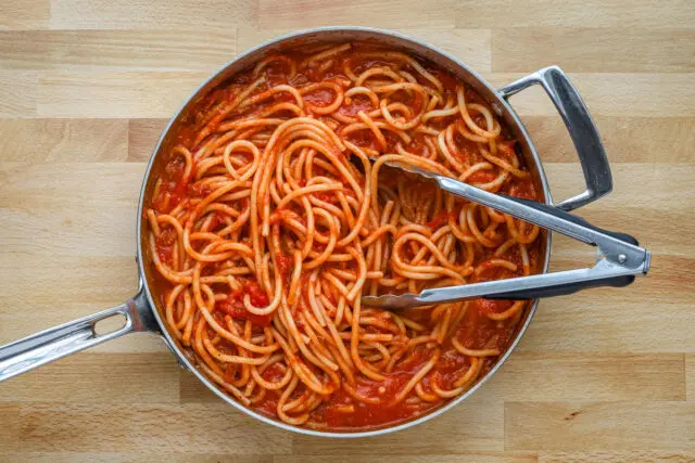 The pasta is added to the sauce and tossed with some of the cooking water to build a saucy mixture.