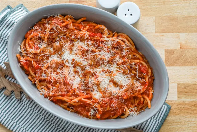 A serving bowl with bucatini all'Amatriciana topped with grated pecorino Romano and extra guanciale.