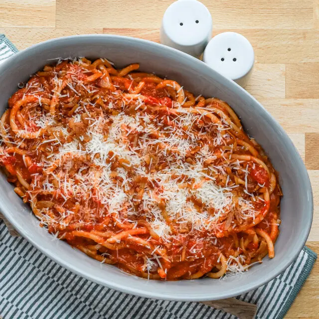 A serving bowl with bucatini all'Amatriciana topped with grated pecorino Romano and extra guanciale.