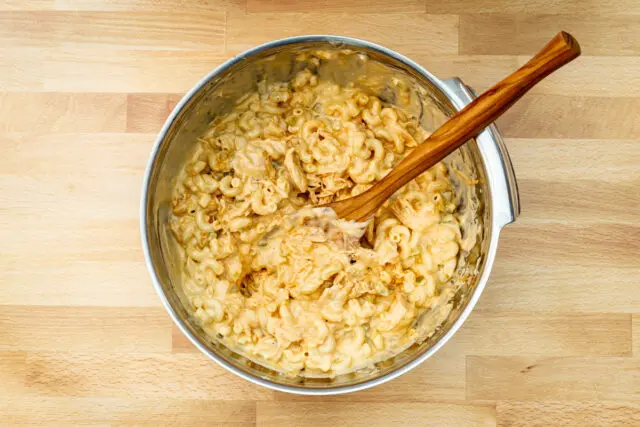 Combining the cheese sauce, chicken mixture, and macaroni for the buffalo chicken mac and cheese.