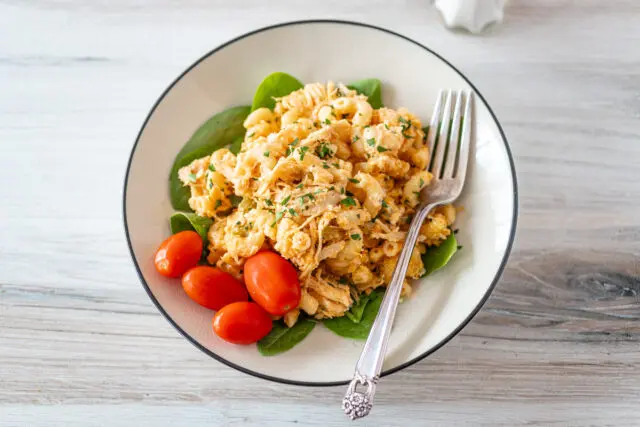 Buffalo chicken mac and cheese on a plate with some parsley and grape tomatoes.