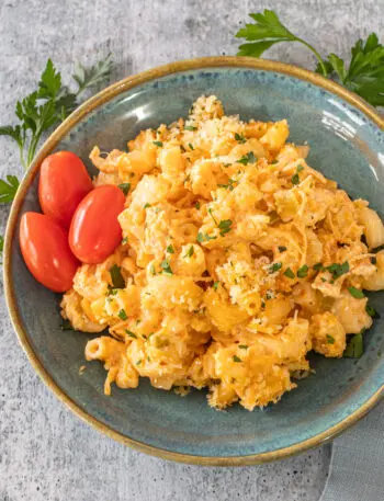 Buffalo chicken mac and cheese on a plate with some parsley and grape tomatoes.