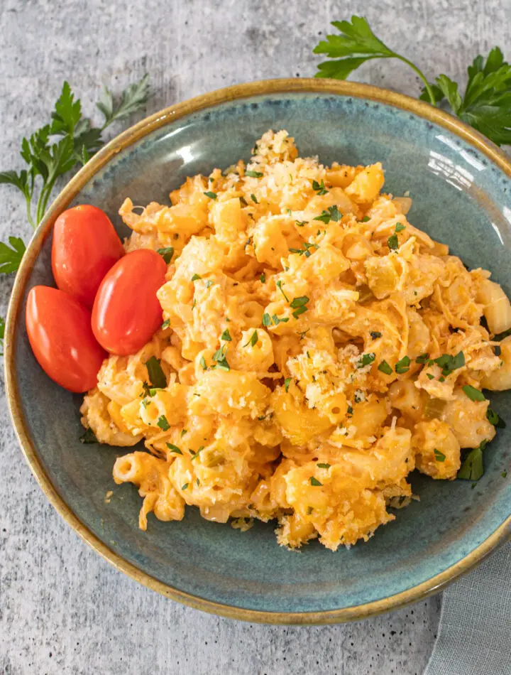 Buffalo chicken mac and cheese on a plate with some parsley and grape tomatoes.