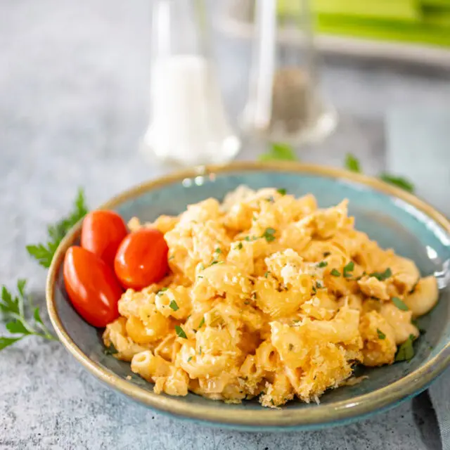 Buffalo chicken mac and cheese on a plate with some parsley and grape tomatoes.