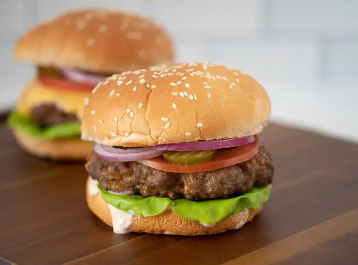 grilled burger with chipotle mayonnaise or aioli on a board with a cheeseburger in the background