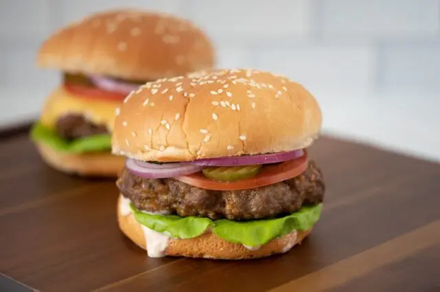 grilled burger with chipotle mayonnaise or aioli on a board with a cheeseburger in the background