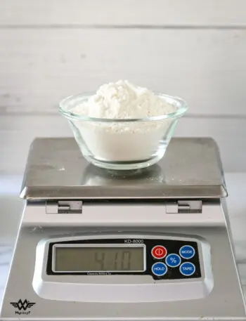 A cup of flour on a scale, making cake flour with all-purpose and cornstarch.