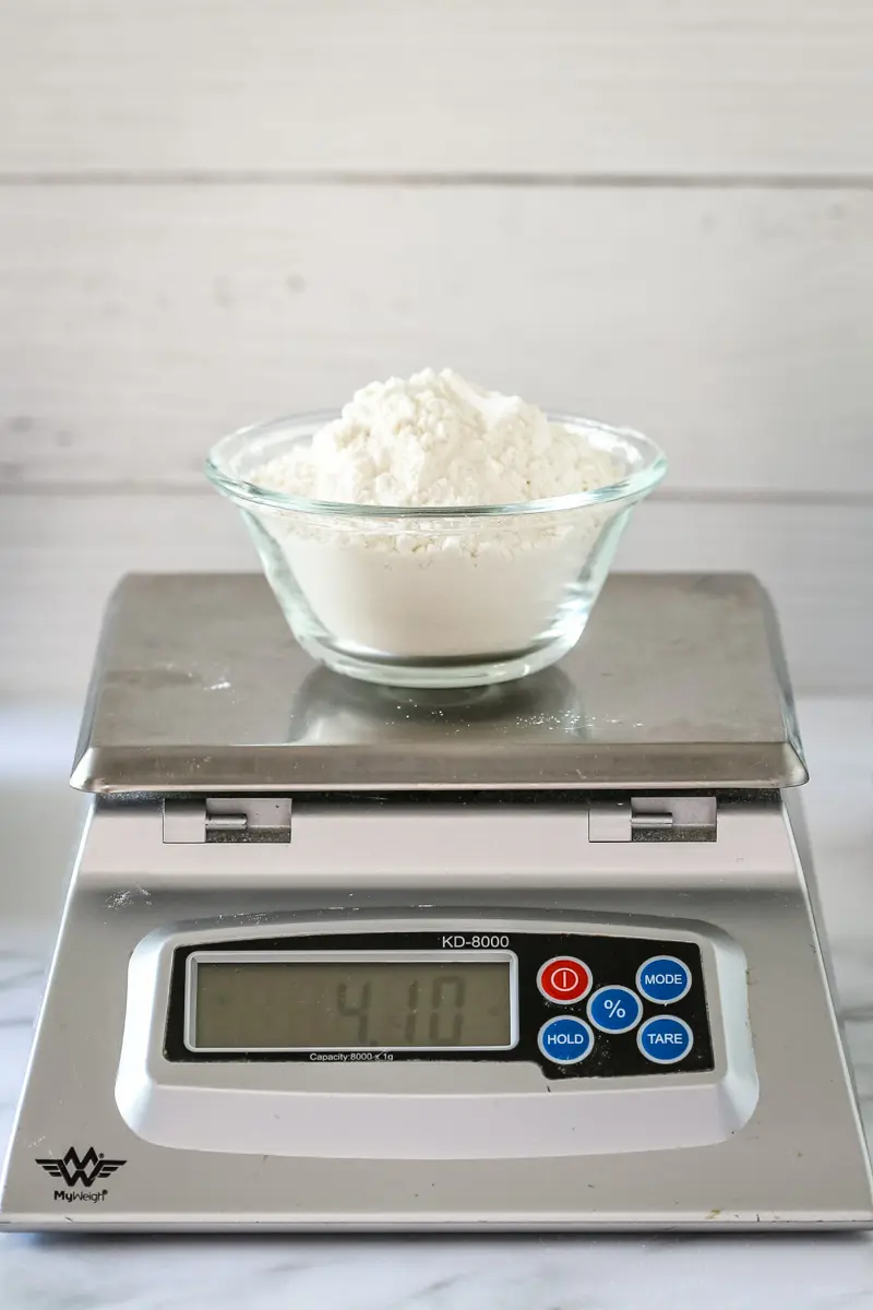 A cup of flour on a scale, making cake flour with all-purpose and cornstarch.