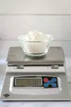 A cup of flour on a scale, making cake flour with all-purpose and cornstarch.